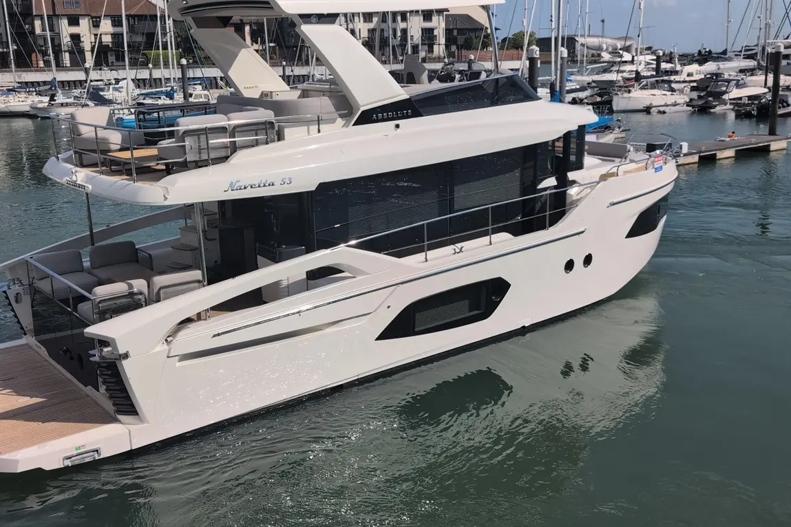A luxury Navetta 53 yacht moored in a marina, showcasing sleek design, outdoor seating, and reflections on calm water.